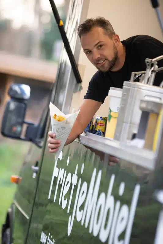 Medewerker van Frietje Mobiel reikt een puntzak friet aan uit de frietwagen